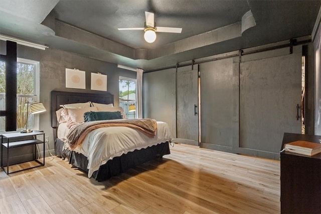 bedroom with ceiling fan, a barn door, light wood-type flooring, and multiple windows