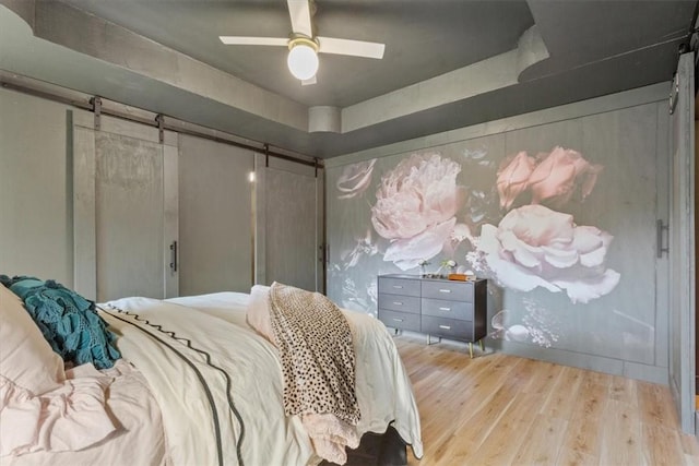 bedroom featuring ceiling fan, a barn door, and light wood-type flooring