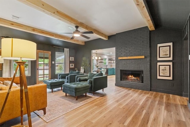 living room featuring wood-type flooring, lofted ceiling with beams, a brick fireplace, and ceiling fan