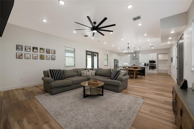 living room with ceiling fan with notable chandelier and light hardwood / wood-style floors