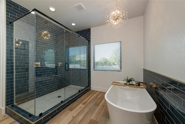 bathroom with separate shower and tub, wood-type flooring, tile walls, and a chandelier