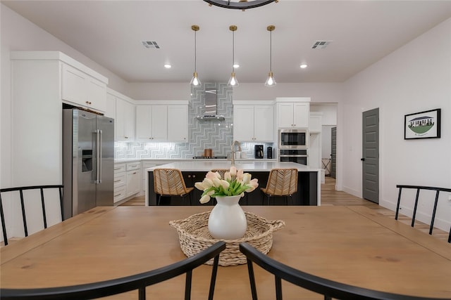 kitchen featuring appliances with stainless steel finishes, white cabinetry, a kitchen island with sink, and wall chimney exhaust hood