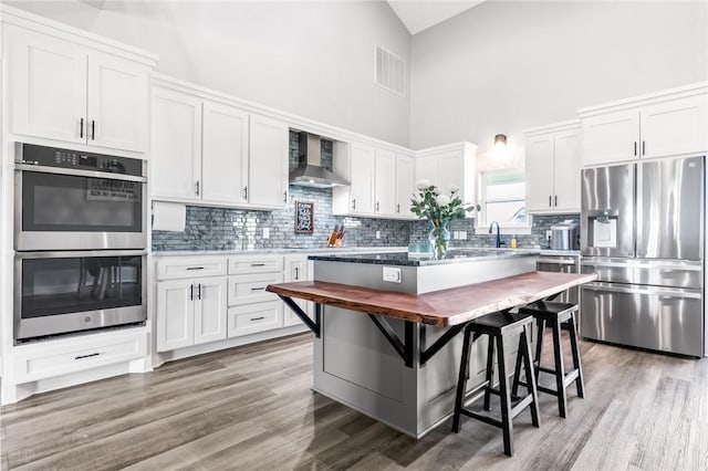 kitchen featuring appliances with stainless steel finishes, wall chimney range hood, and white cabinetry