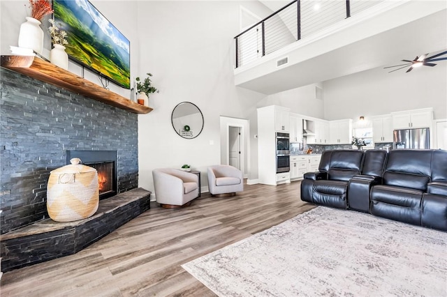 living room featuring ceiling fan, wood-type flooring, a fireplace, and a high ceiling