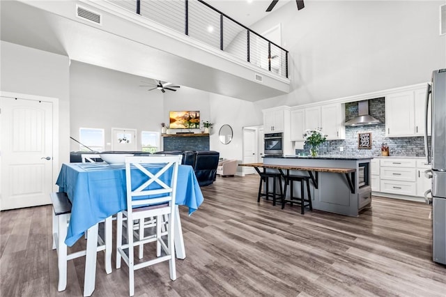 kitchen with high vaulted ceiling, wall chimney range hood, white cabinets, and oven