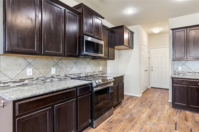 kitchen with backsplash, light stone counters, light hardwood / wood-style floors, and appliances with stainless steel finishes