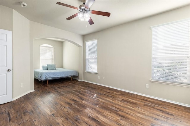 unfurnished bedroom featuring multiple windows, dark wood-type flooring, and ceiling fan