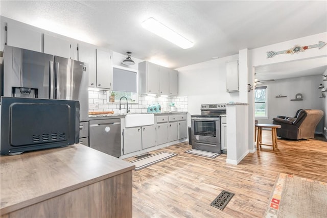 kitchen featuring sink, backsplash, gray cabinetry, light hardwood / wood-style floors, and stainless steel appliances