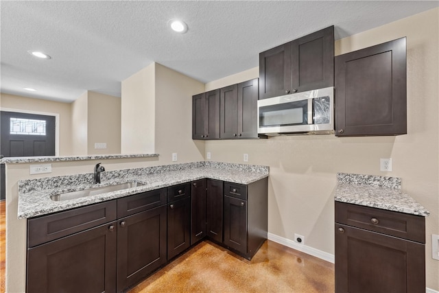 kitchen featuring a textured ceiling, stainless steel microwave, a sink, and light stone countertops