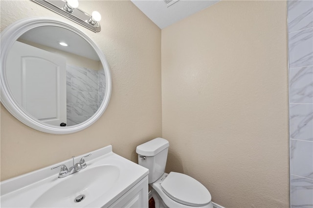 bathroom with a textured wall, vanity, and toilet