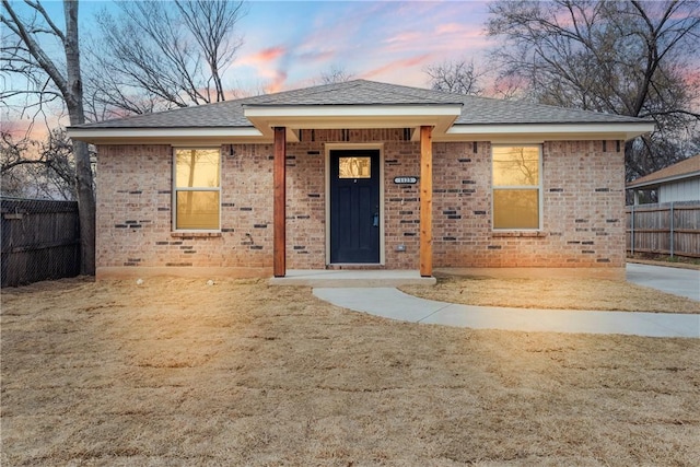 ranch-style house featuring a shingled roof, fence, and brick siding