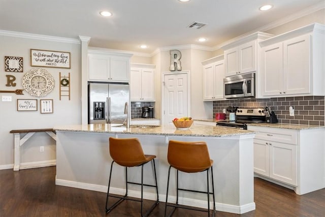 kitchen featuring appliances with stainless steel finishes, white cabinetry, a kitchen island with sink, and light stone counters