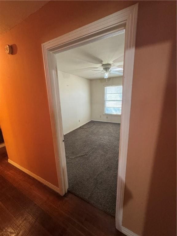 corridor featuring dark colored carpet, dark wood finished floors, and baseboards