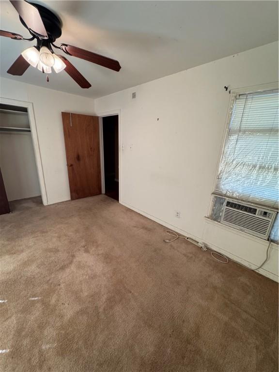 unfurnished bedroom with light carpet, cooling unit, a ceiling fan, and a closet