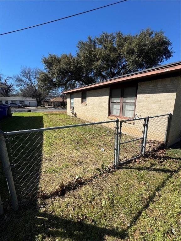 view of property exterior featuring brick siding, a lawn, fence, and a gate