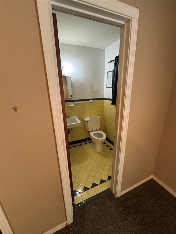 half bath featuring tile walls, toilet, wainscoting, a sink, and tile patterned floors