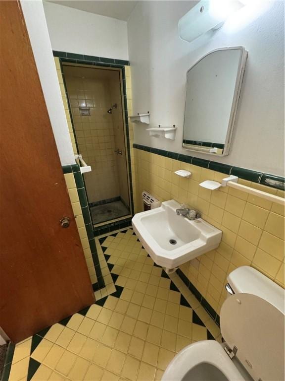 full bath featuring toilet, a sink, tile walls, wainscoting, and a stall shower