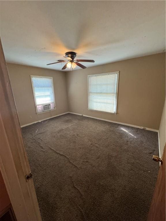 empty room with dark colored carpet, cooling unit, a ceiling fan, and baseboards