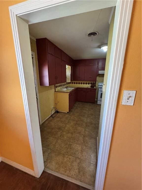 kitchen with visible vents, stove, a sink, under cabinet range hood, and baseboards