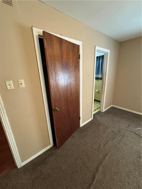 unfurnished bedroom with connected bathroom, a closet, dark carpet, and baseboards