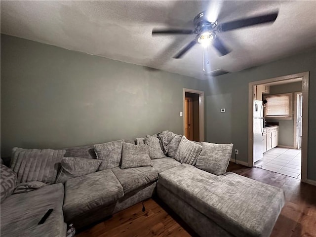 living room with ceiling fan, light wood-type flooring, and a textured ceiling