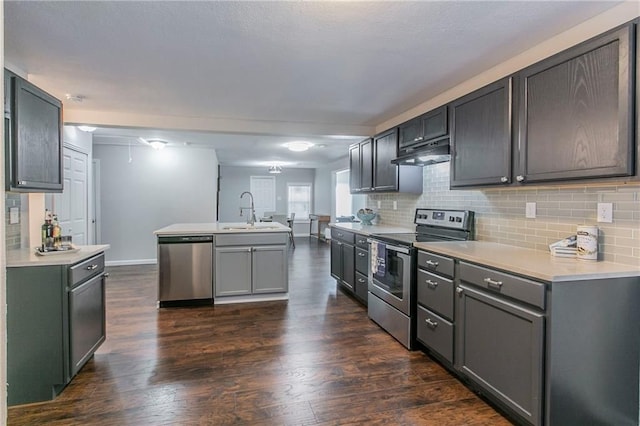 kitchen featuring dark wood-type flooring, sink, an island with sink, appliances with stainless steel finishes, and tasteful backsplash