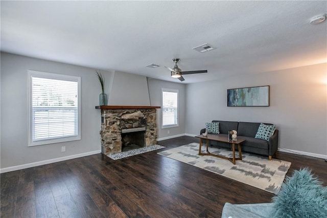 living room with dark hardwood / wood-style flooring, a stone fireplace, and ceiling fan