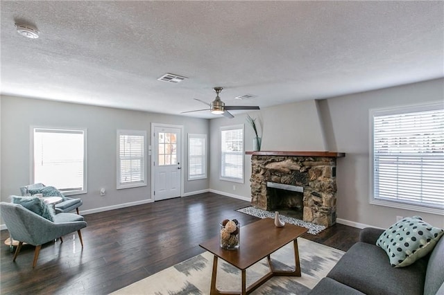 living room with a stone fireplace, ceiling fan, dark wood-type flooring, and a textured ceiling