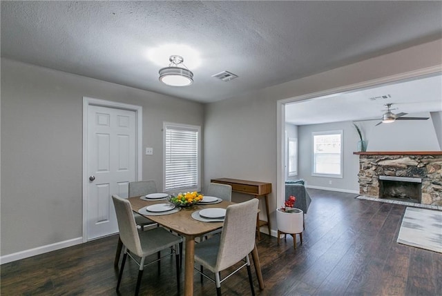 dining room with a stone fireplace, ceiling fan, dark hardwood / wood-style flooring, and a textured ceiling