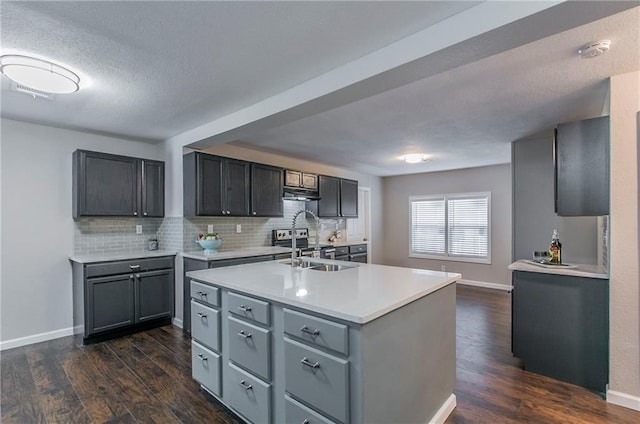 kitchen featuring a textured ceiling, dark hardwood / wood-style floors, sink, and an island with sink