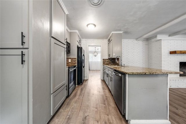 kitchen featuring gray cabinetry, stone counters, light wood-type flooring, appliances with stainless steel finishes, and brick wall