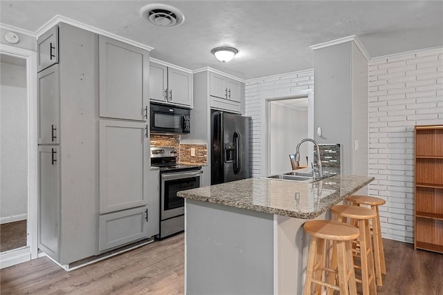 kitchen with hardwood / wood-style floors, black appliances, sink, gray cabinets, and light stone countertops