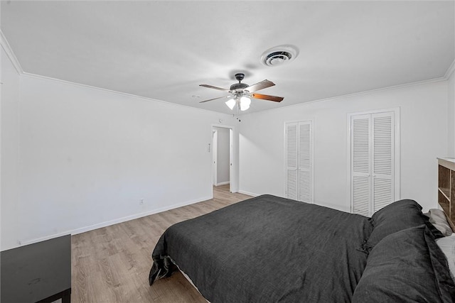 bedroom featuring two closets, light hardwood / wood-style floors, ceiling fan, and ornamental molding