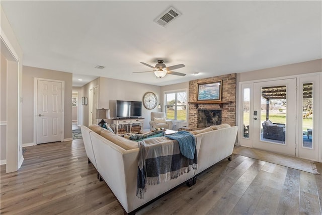 living room featuring visible vents, a brick fireplace, baseboards, and wood finished floors