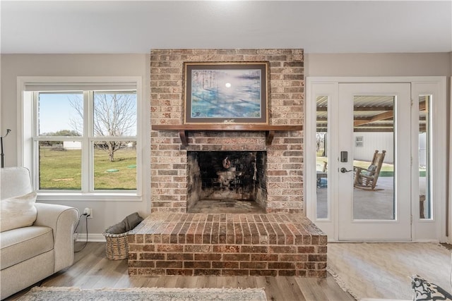 living area featuring a brick fireplace, wood finished floors, and baseboards