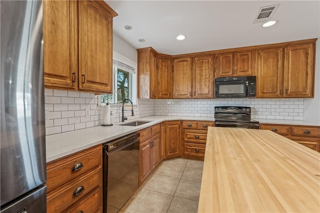 kitchen featuring visible vents, butcher block counters, light tile patterned floors, brown cabinets, and black appliances