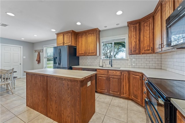 kitchen featuring visible vents, black appliances, a sink, a kitchen island, and light countertops