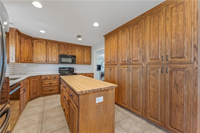 kitchen with butcher block counters, light tile patterned floors, decorative backsplash, brown cabinetry, and black appliances