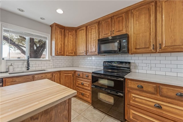 kitchen featuring butcher block countertops, light tile patterned floors, brown cabinets, black appliances, and a sink