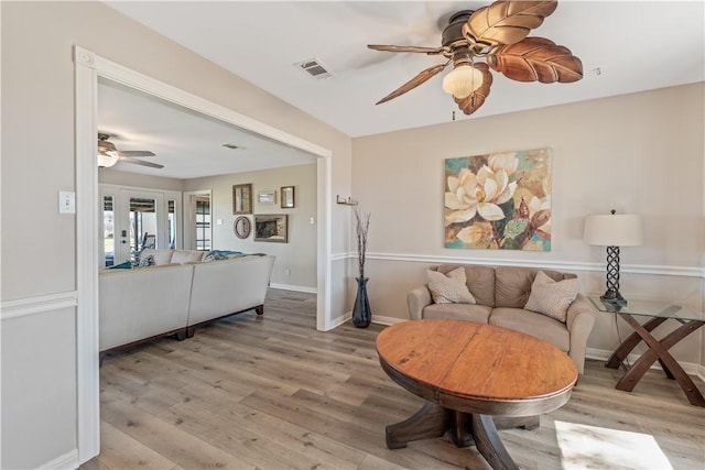 living room with visible vents, baseboards, ceiling fan, and light wood finished floors