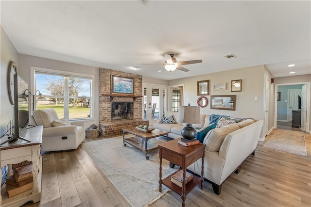 living room with visible vents, light wood-style floors, a fireplace, baseboards, and ceiling fan