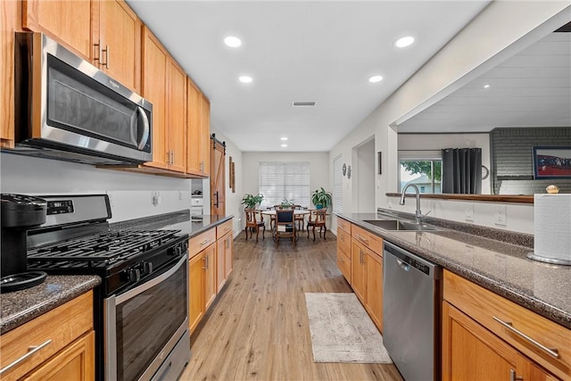 kitchen featuring dark stone counters, sink, stainless steel appliances, and light hardwood / wood-style flooring