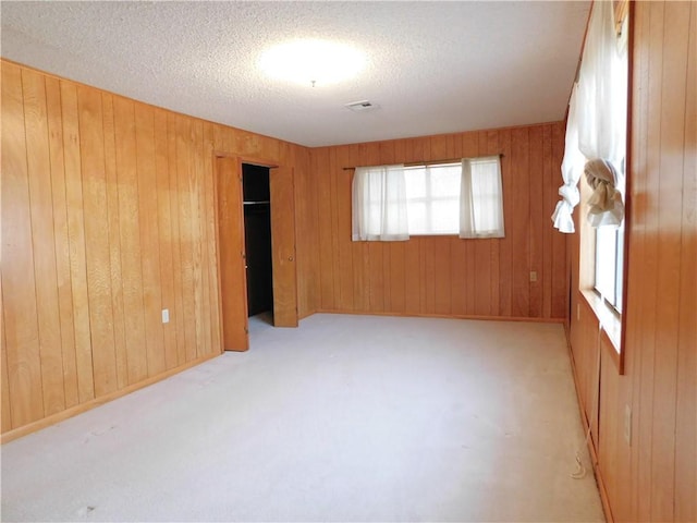 unfurnished room with carpet floors, wooden walls, visible vents, and a textured ceiling