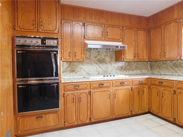 kitchen with brown cabinets, under cabinet range hood, dobule oven black, and light countertops