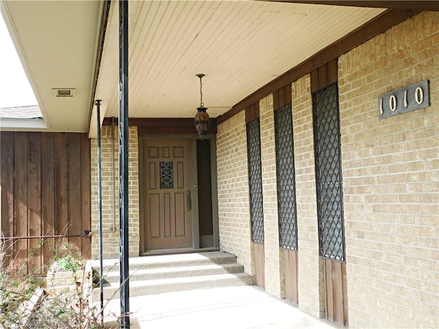 property entrance with covered porch, visible vents, and brick siding