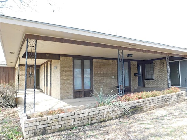 doorway to property featuring covered porch and brick siding