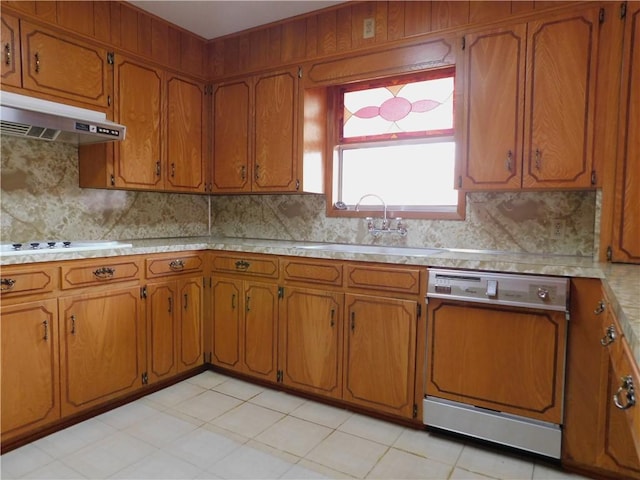 kitchen featuring under cabinet range hood, paneled dishwasher, brown cabinetry, and a sink