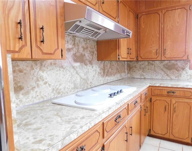 kitchen with decorative backsplash, white electric cooktop, brown cabinets, light countertops, and under cabinet range hood