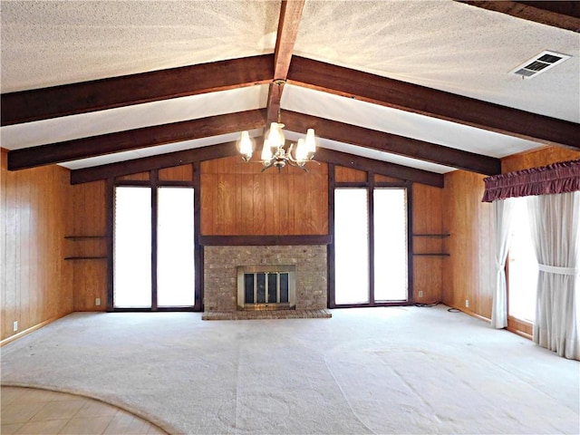 unfurnished living room featuring wooden walls, visible vents, a textured ceiling, a brick fireplace, and a chandelier