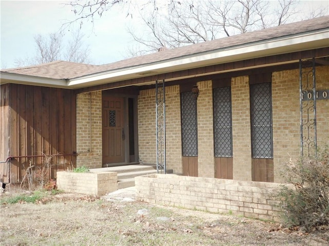 entrance to property featuring roof with shingles and brick siding